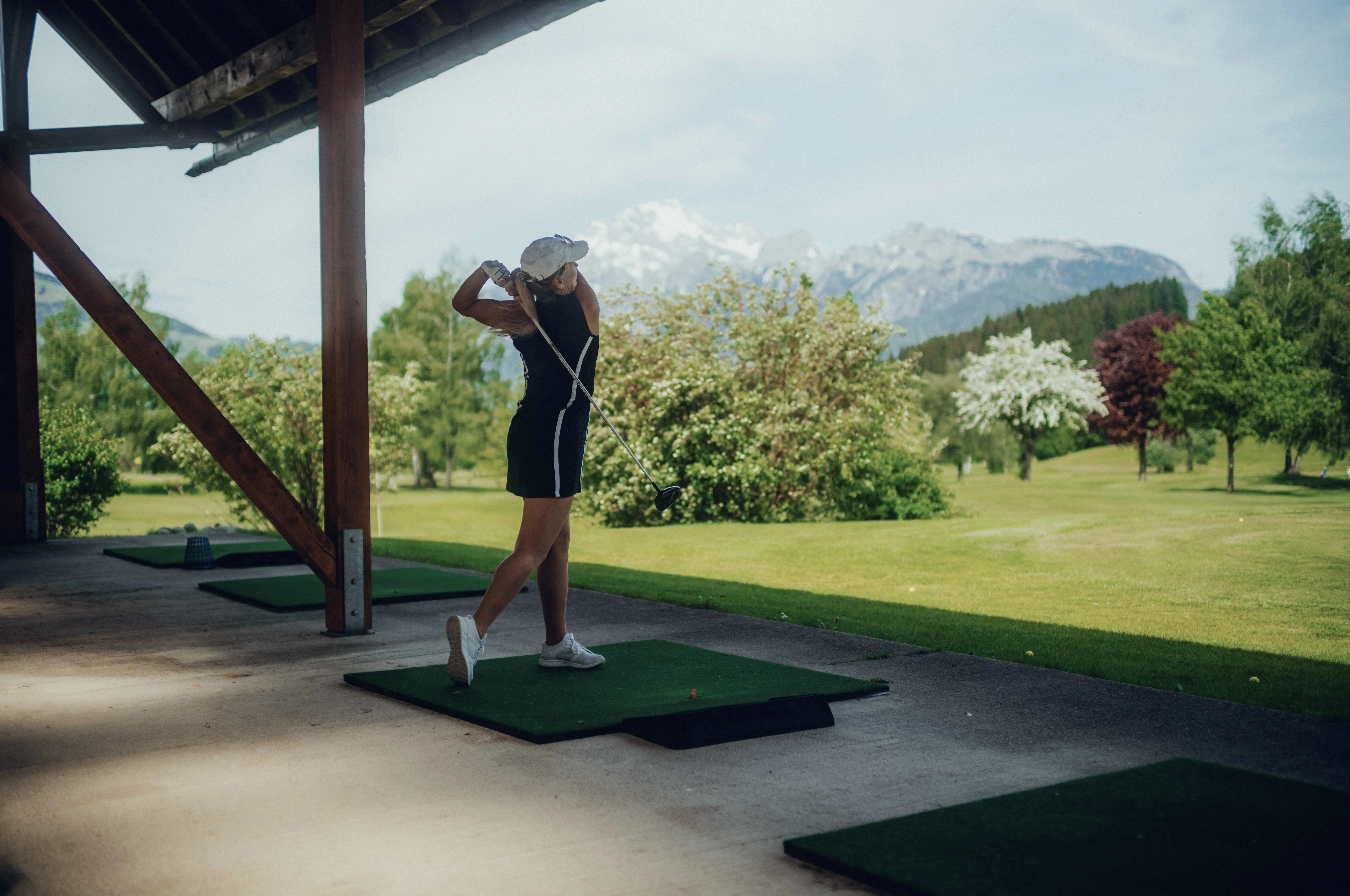 Sportler schlägt Golfball auf Übungsbereich mit Bergen im Hintergrund