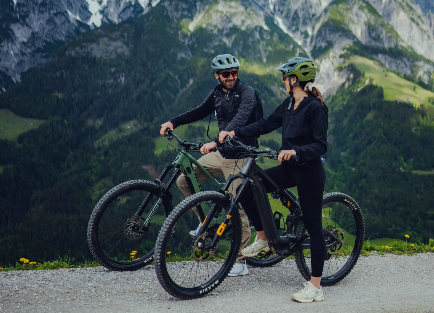 Paar mit Mountainbikes vor Bergen und grüner Landschaft