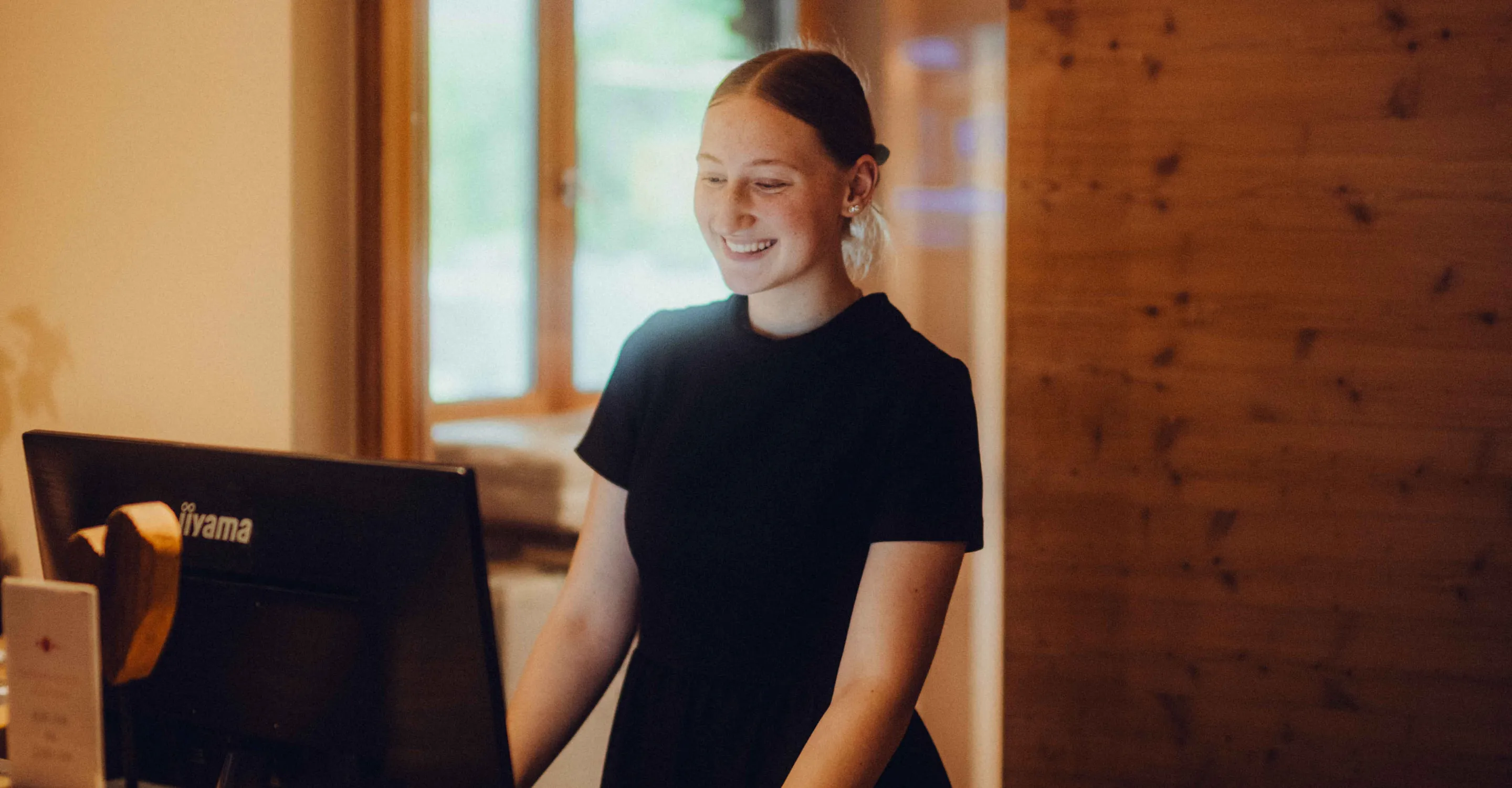 Smiling person at a computer in a bright room.