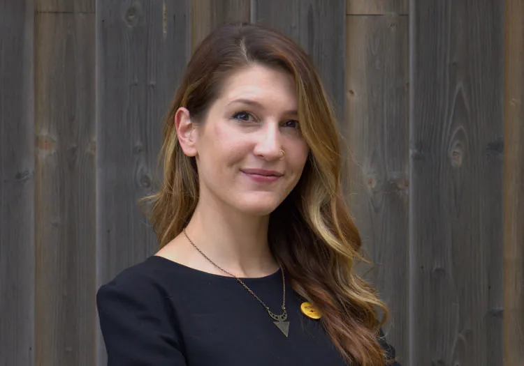 Frau in schwarzem Oberteil mit goldener Kette vor einer Holzwand