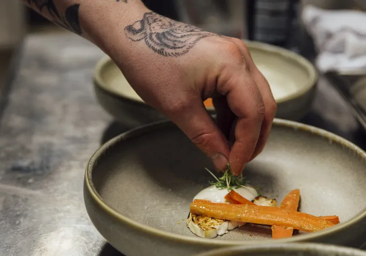 Hand eines Kochs, der ein Gericht in einer Schüssel anrichtet