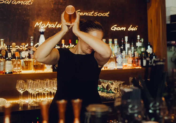 Barkeeper schüttelt einen Cocktail an einer Bar mit verschiedenen Flaschen im Hintergrund
