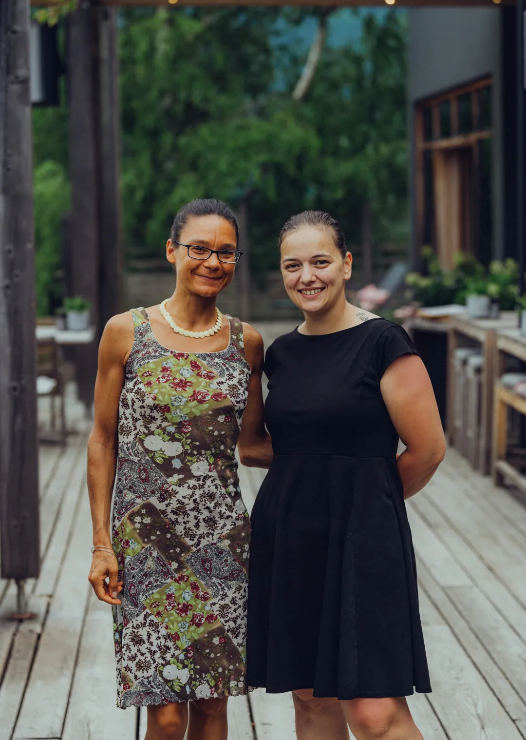 Zwei Frauen posieren draußen auf einer Holzterrasse
