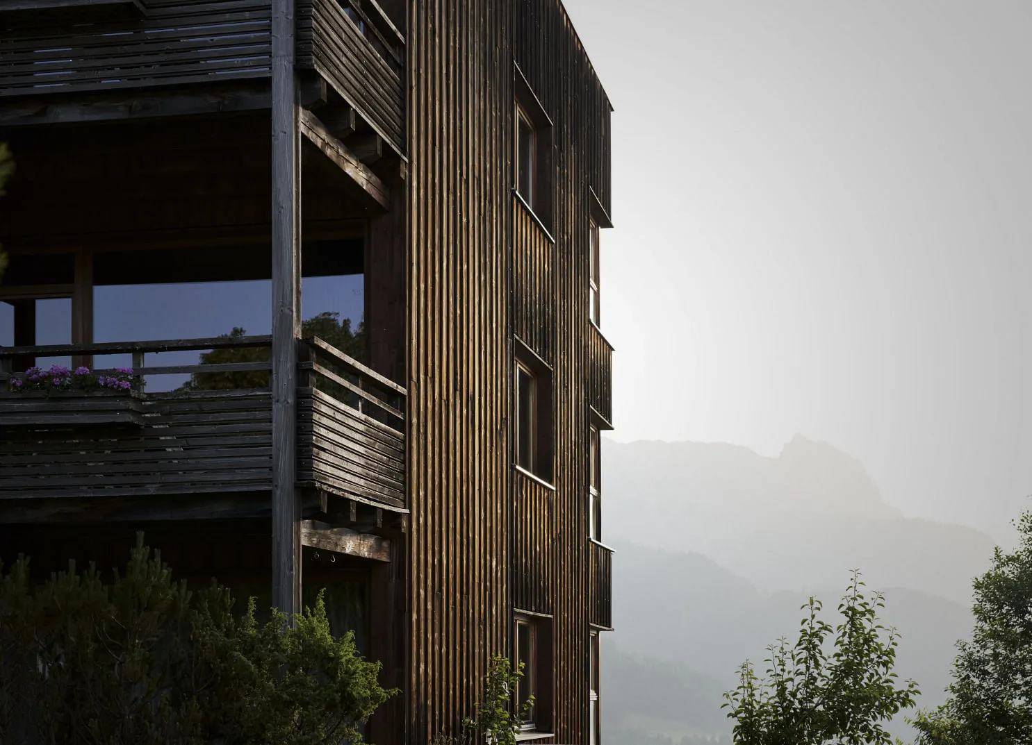 Holzgebäude mit Balkonen, Berge im Hintergrund, neblige Atmosphäre