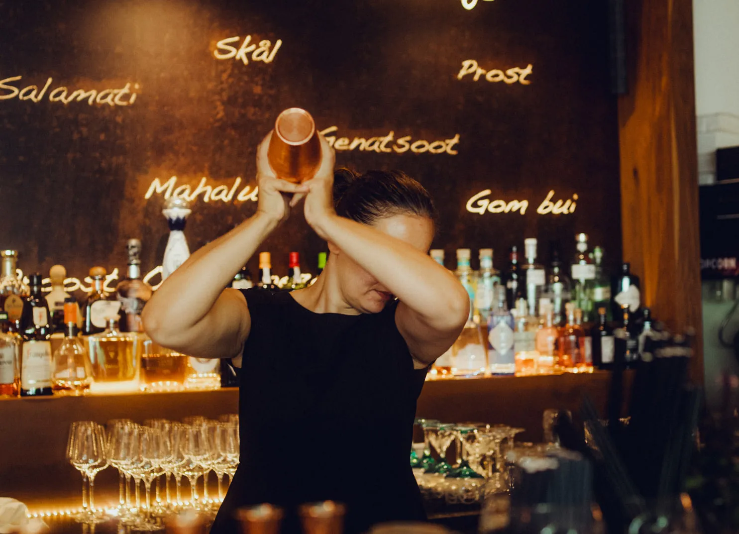 Barkeeper schüttelt einen Cocktail mit einer Barregal voller Flaschen im Hintergrund