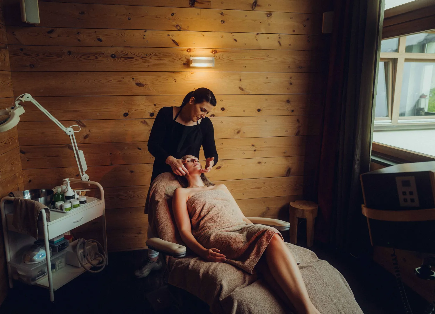 Woman receiving a facial treatment in a spa with wooden walls.