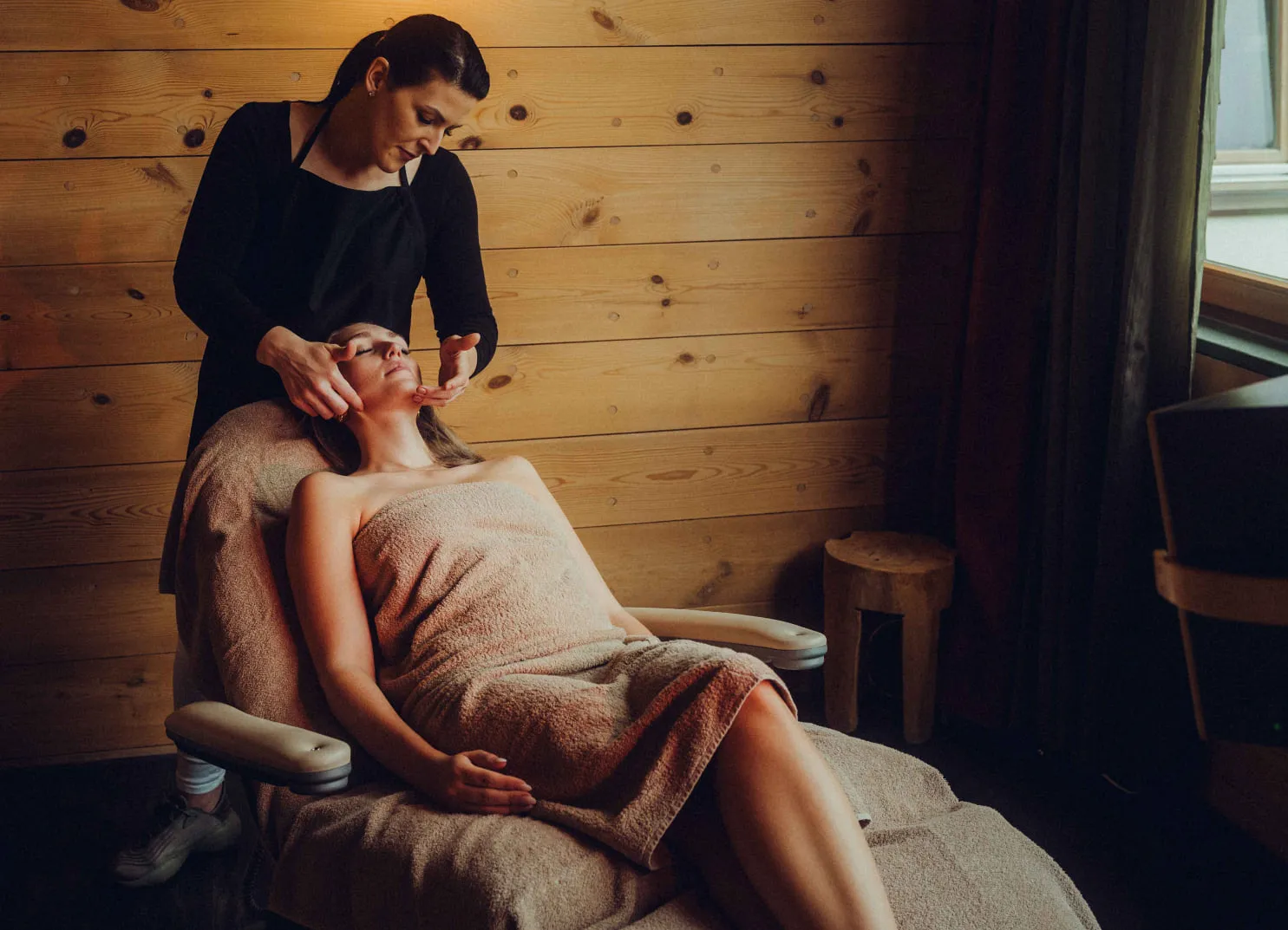 Eine Frau erhält eine Gesichtsbehandlung in einem Spa-Raum mit Holzverkleidung.