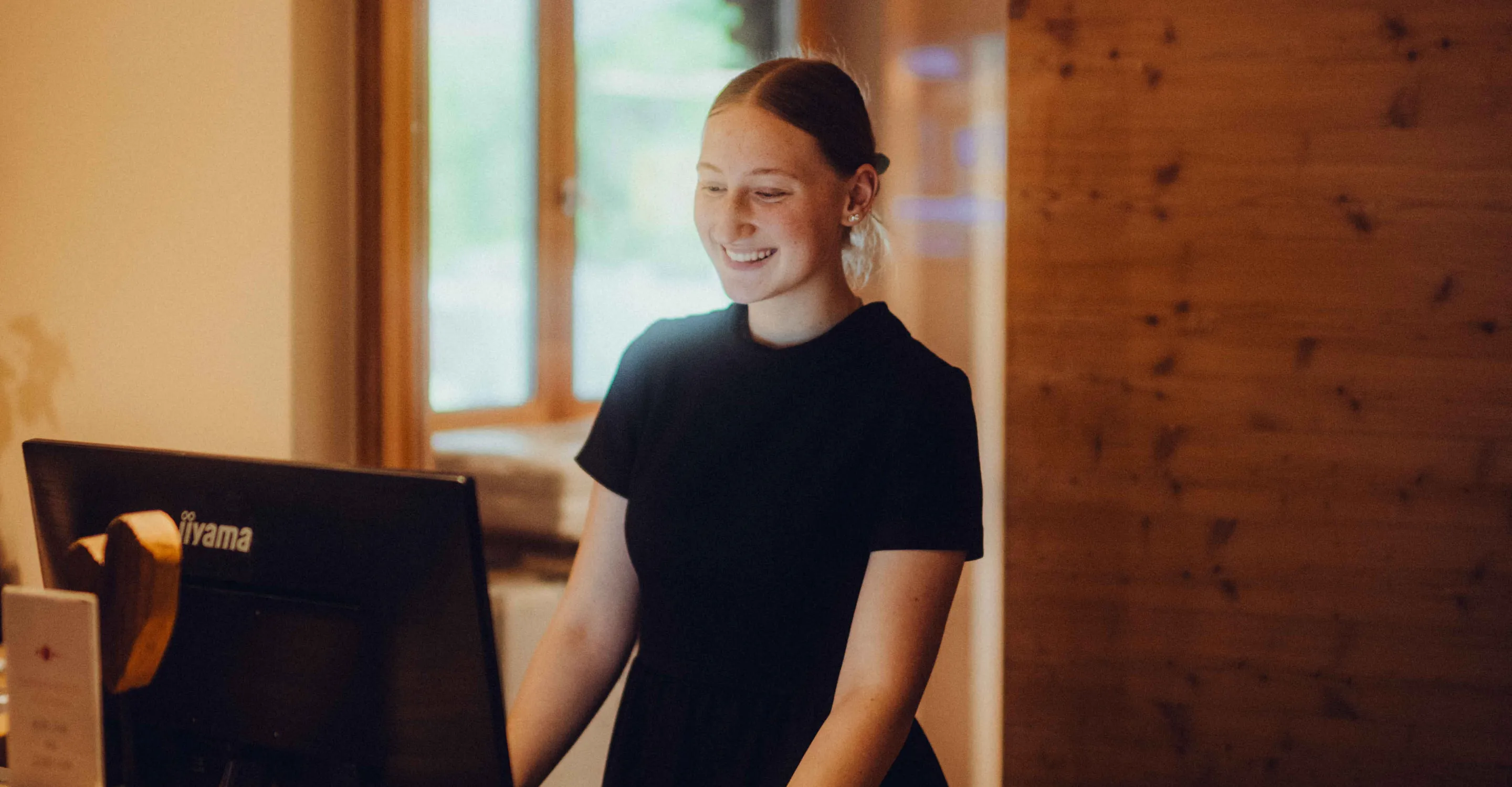 Smiling person stands in front of a computer in a room.