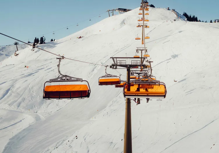 Sesselbahn mit orangefarbenen Sitzplätzen über schneebedecktem Berg