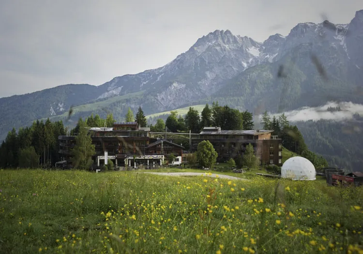 Blick auf ein modernes Gebäude in einer Berglandschaft mit Blumenwiese