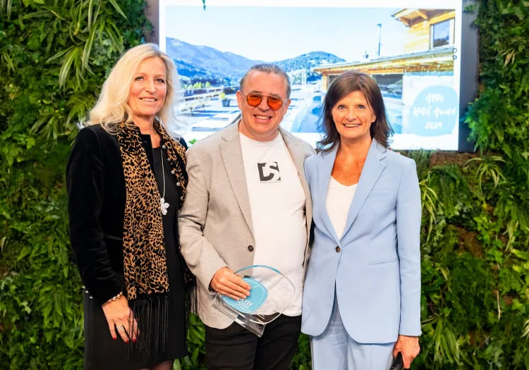 Drei Personen posieren lächelnd vor einem grünen Hintergrund.