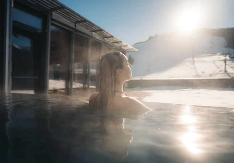 Frau im Außenwhirlpool des Holzhotels Forsth, schneebedeckte Landschaft im Hintergrund