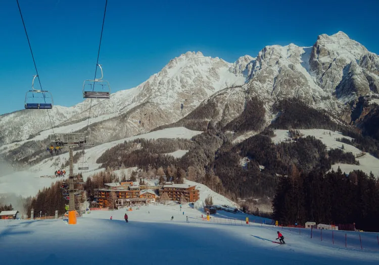 Skigebiet mit Sessellift und Holzhotel im Vordergrund vor einer Berglandschaft