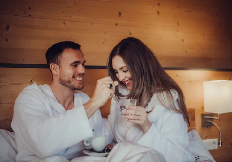Paar in Bademänteln, das in einem Bett sitzt und zusammen Tee trinkt