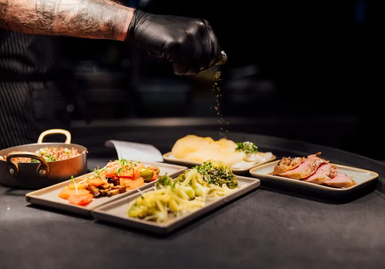 Koch streut Gewürze über mehrere Teller mit verschiedenen Gerichten