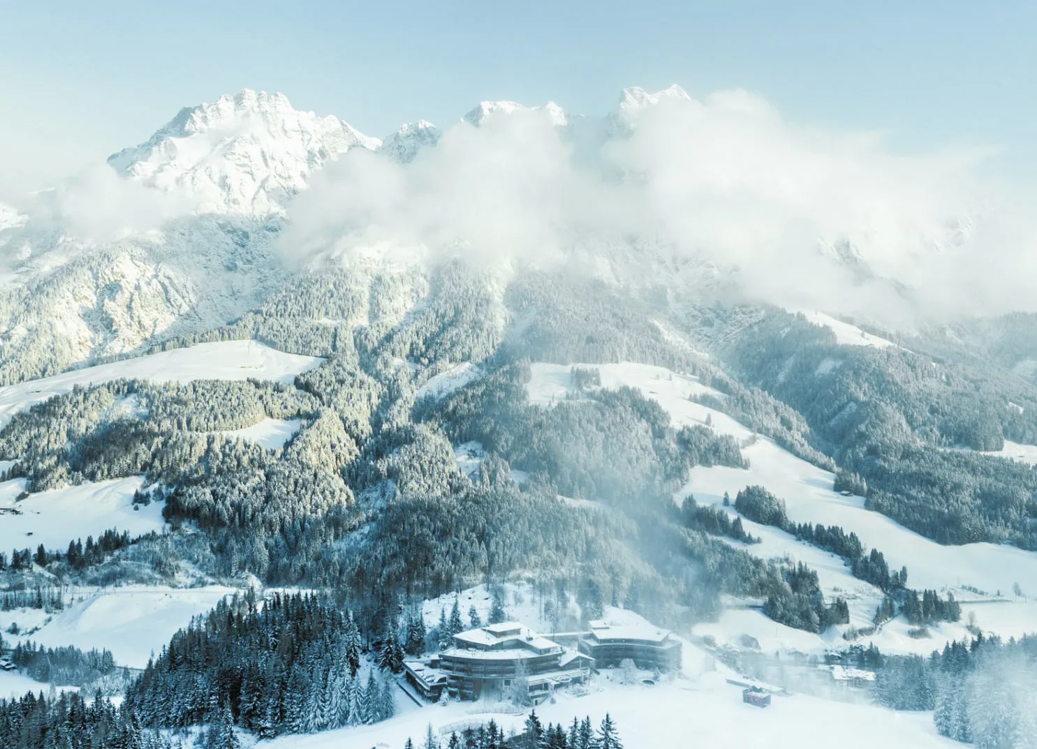 Berglandschaft mit dem Holzhotel Forsthofalm in Leogang und verschneiten Wäldern