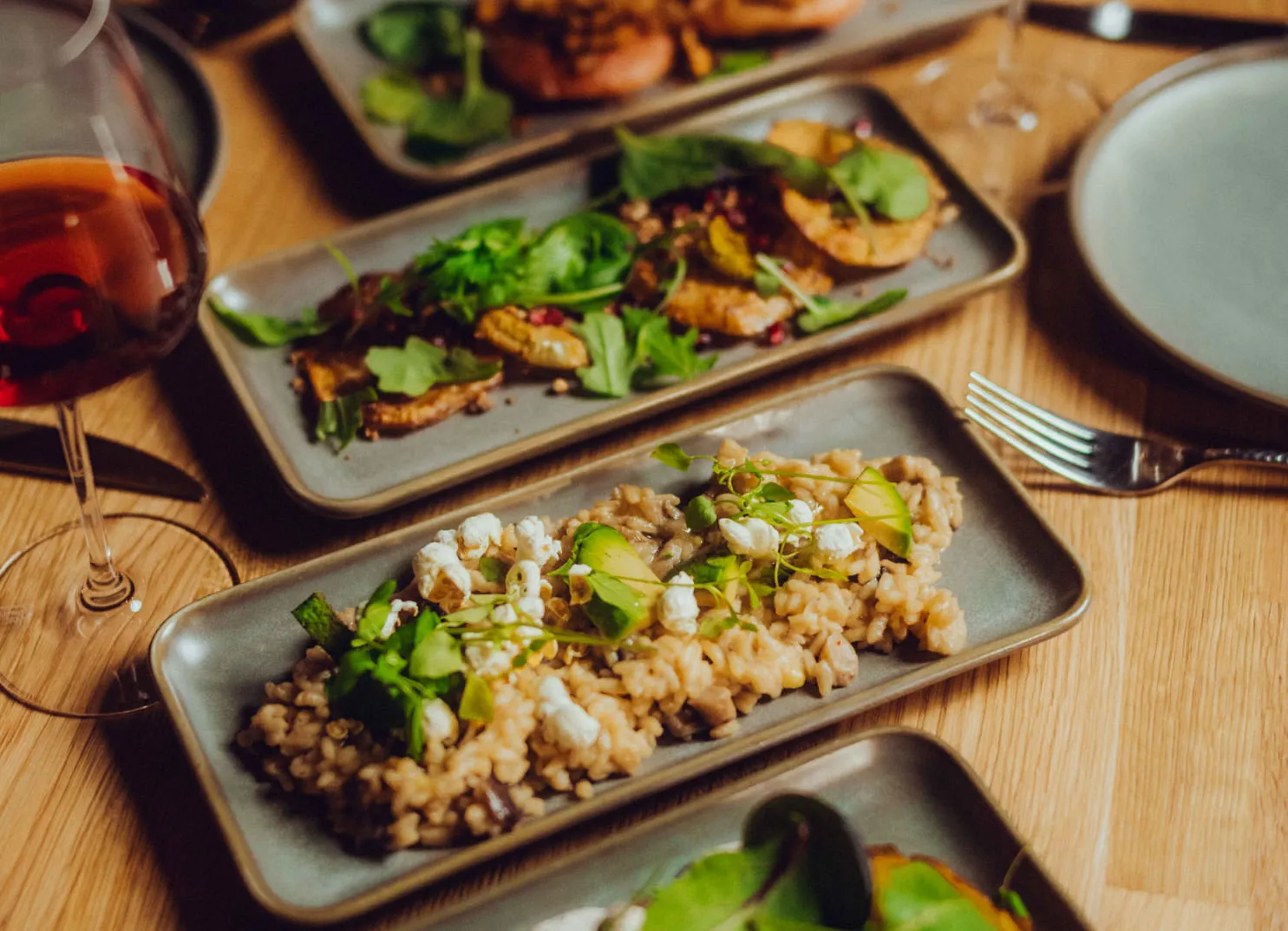 Teller mit Risotto und frischen Kräutern, daneben Weinglas und weitere Speisen.