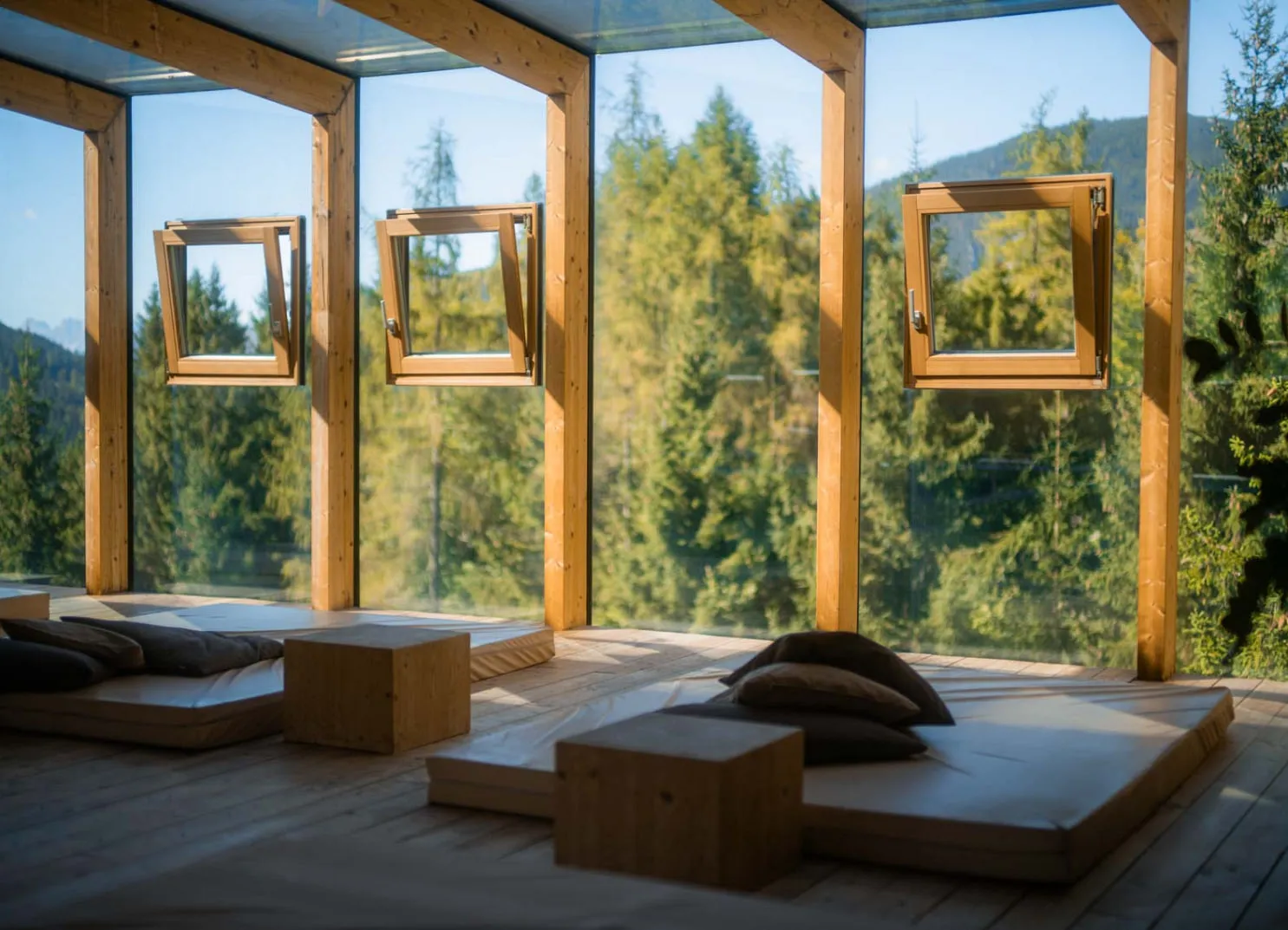Lounge-Bereich im Holzhotel Forsthofalm mit großen Fenstern und Sitzkissen.