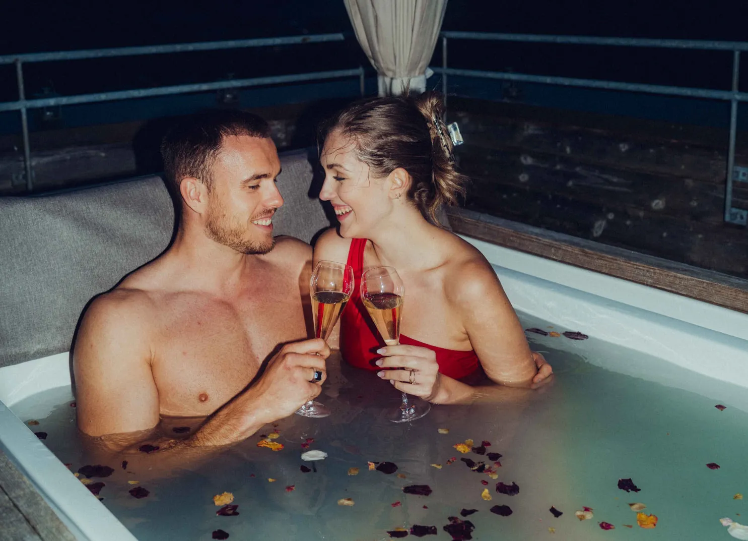 Couple relaxing in a romantic hot tub at night with cocktails.