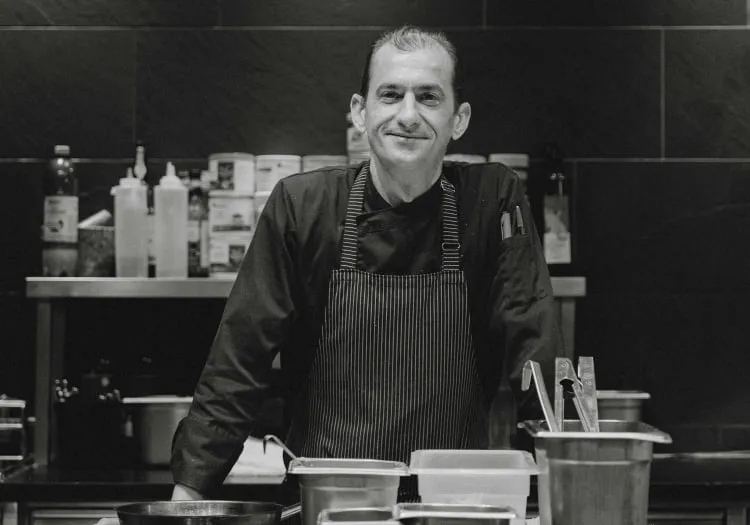 Chef standing in a kitchen with various cooking supplies in the background