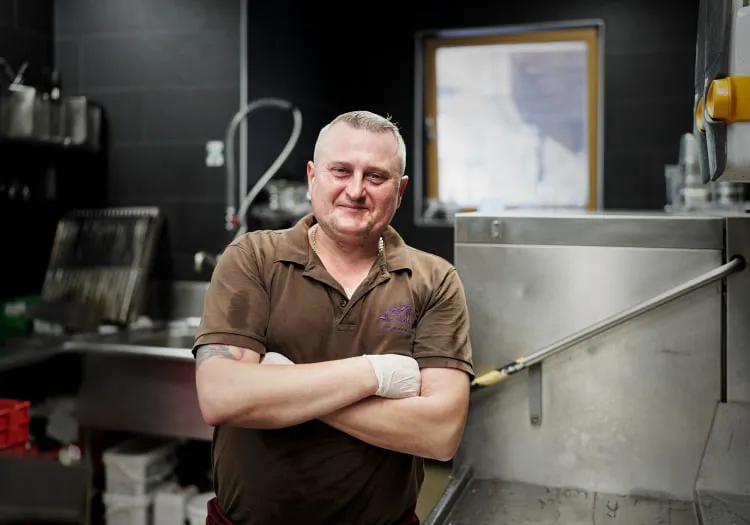 Man in a kitchen standing by a large stainless steel sink.