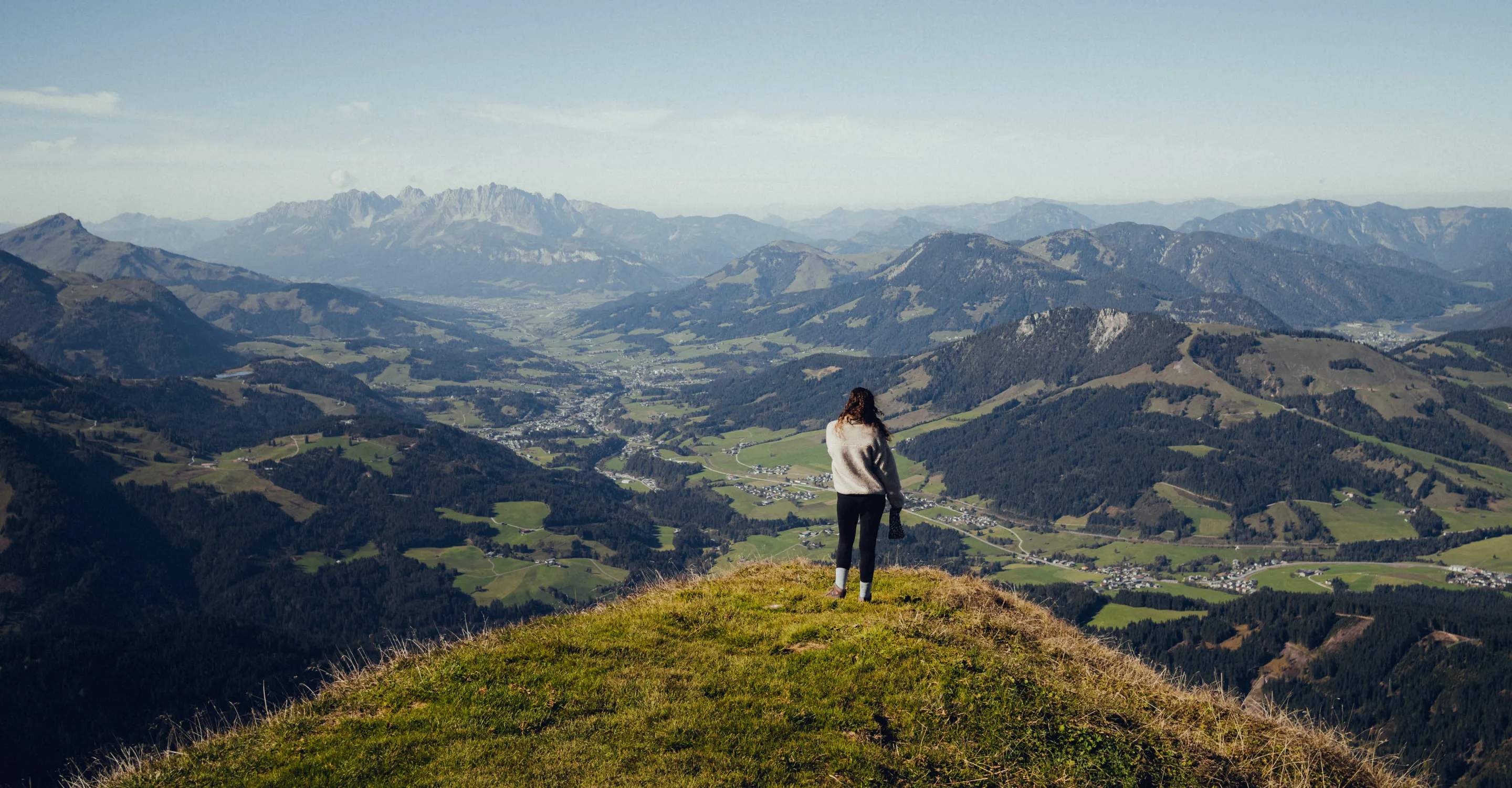 Person steht auf einem Hügel mit Aussicht auf das Tal.