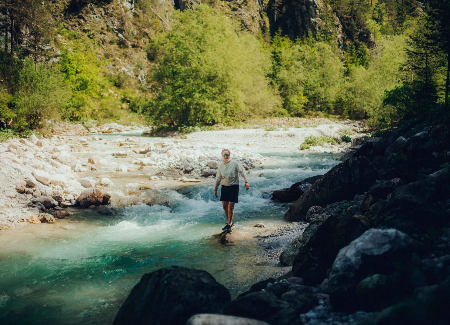 Wanderer überquert einen Bach in einer grünen Landschaft