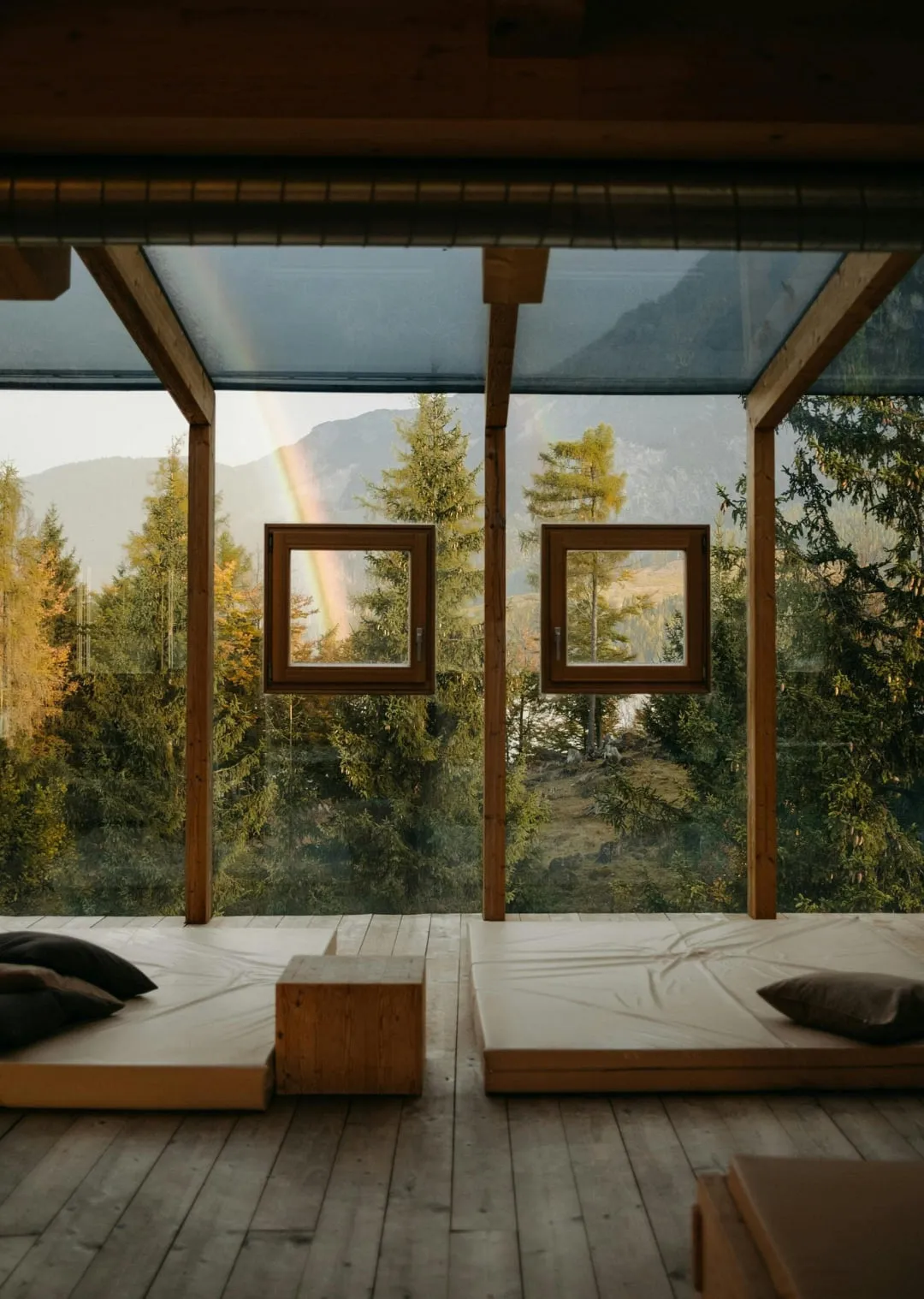 Helle Holzhütte mit großen Fenstern und Blick auf Bäume und Berge.