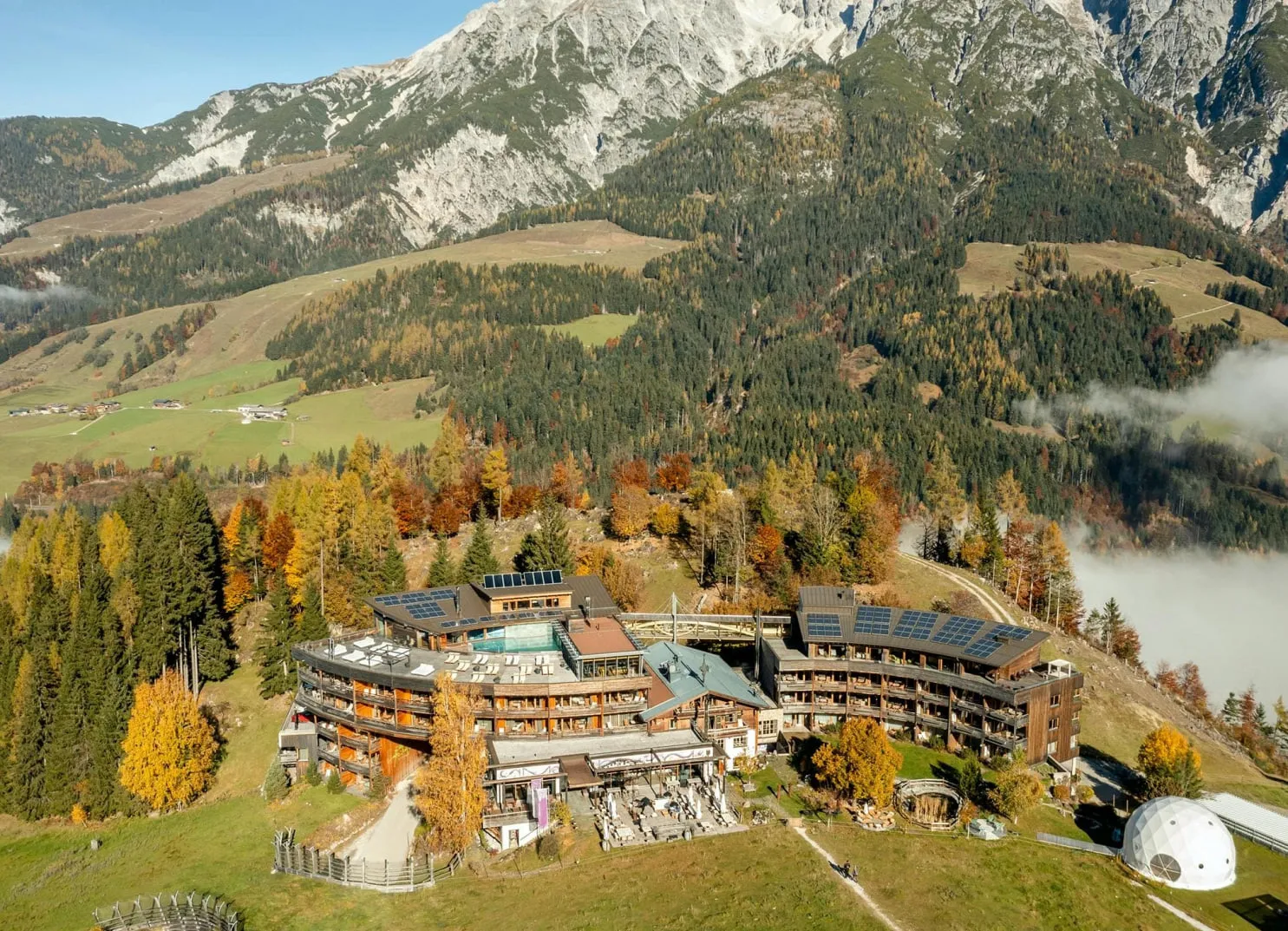 Luftaufnahme eines Hotels in einer bergigen Landschaft mit bunten Bäumen.