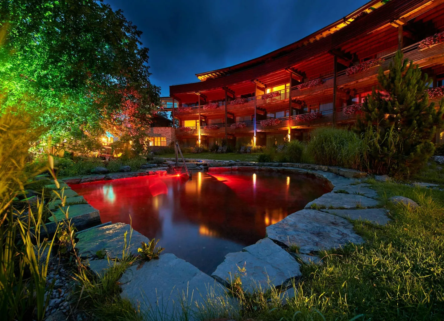 Landschaft mit beleuchtetem Teich und modernem Gebäude bei Nacht
