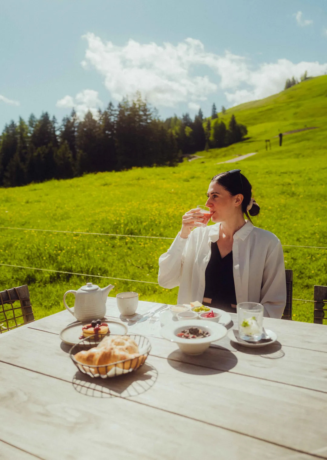 Frau sitzt an Tisch im Freien mit Frühstück in der Natur, Holzhotel Forsthofalm