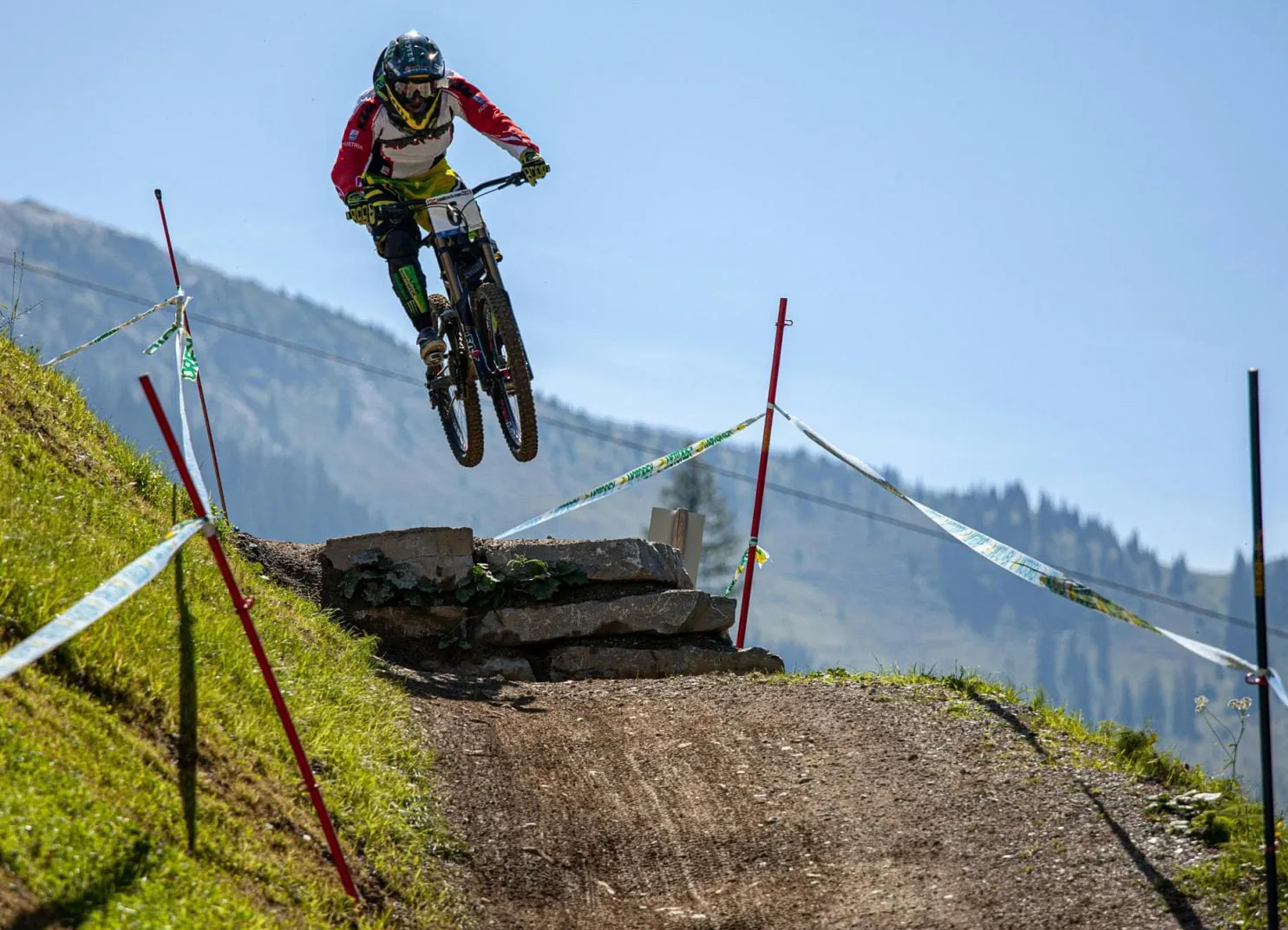 Mountainbiker springt über einen felsigen Pfad mit Bäumen und Bergen im Hintergrund