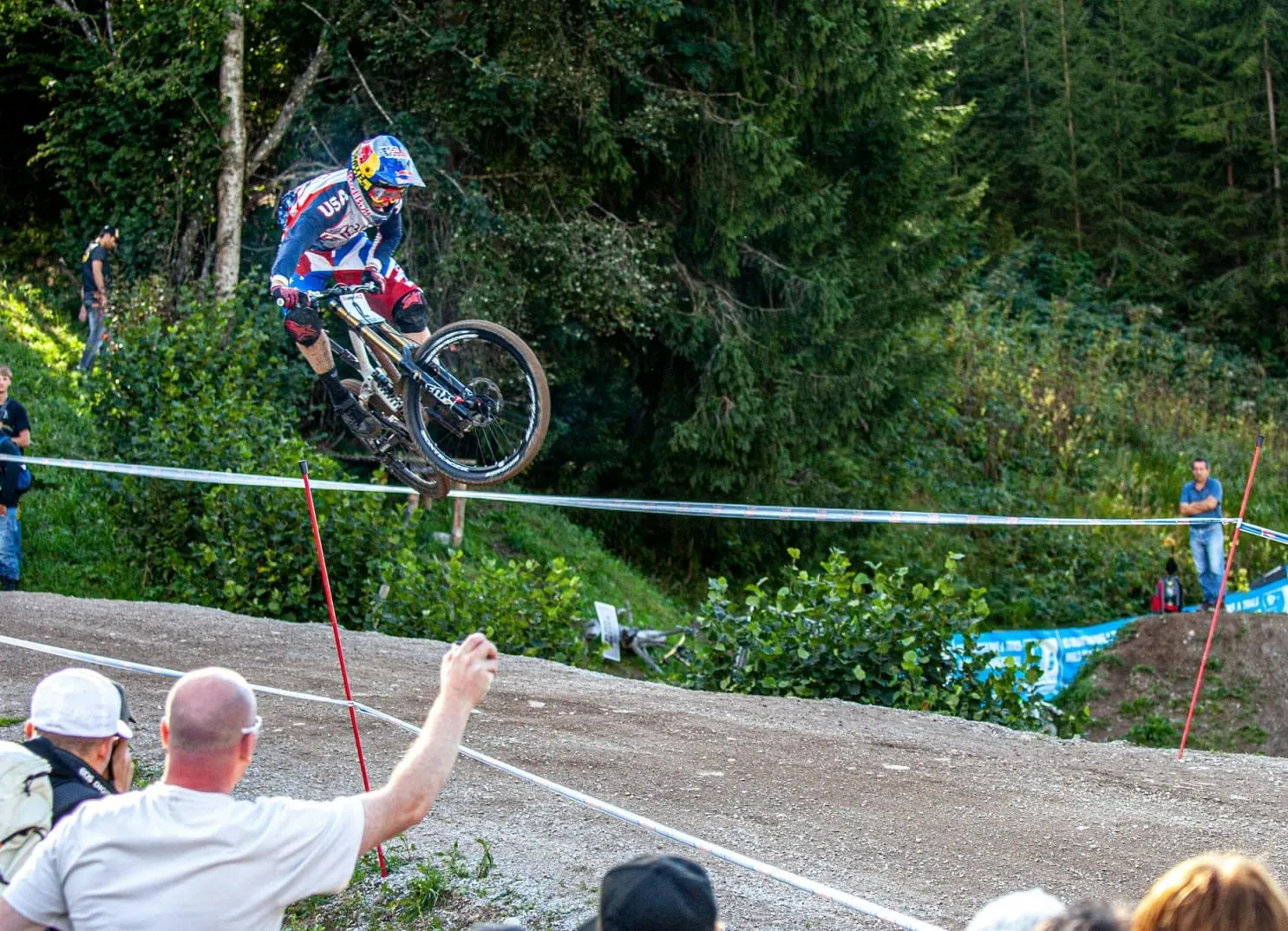 Mountainbiker springt über eine Strecke mit Zuschauern im Vordergrund.