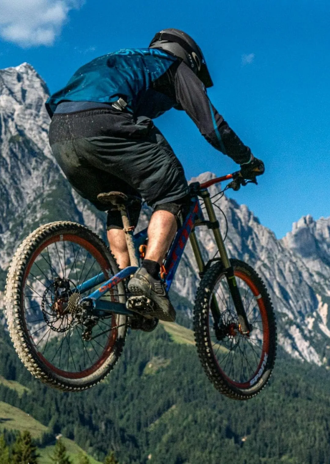 Mountainbiker springt über einen Hügel mit Bergen im Hintergrund