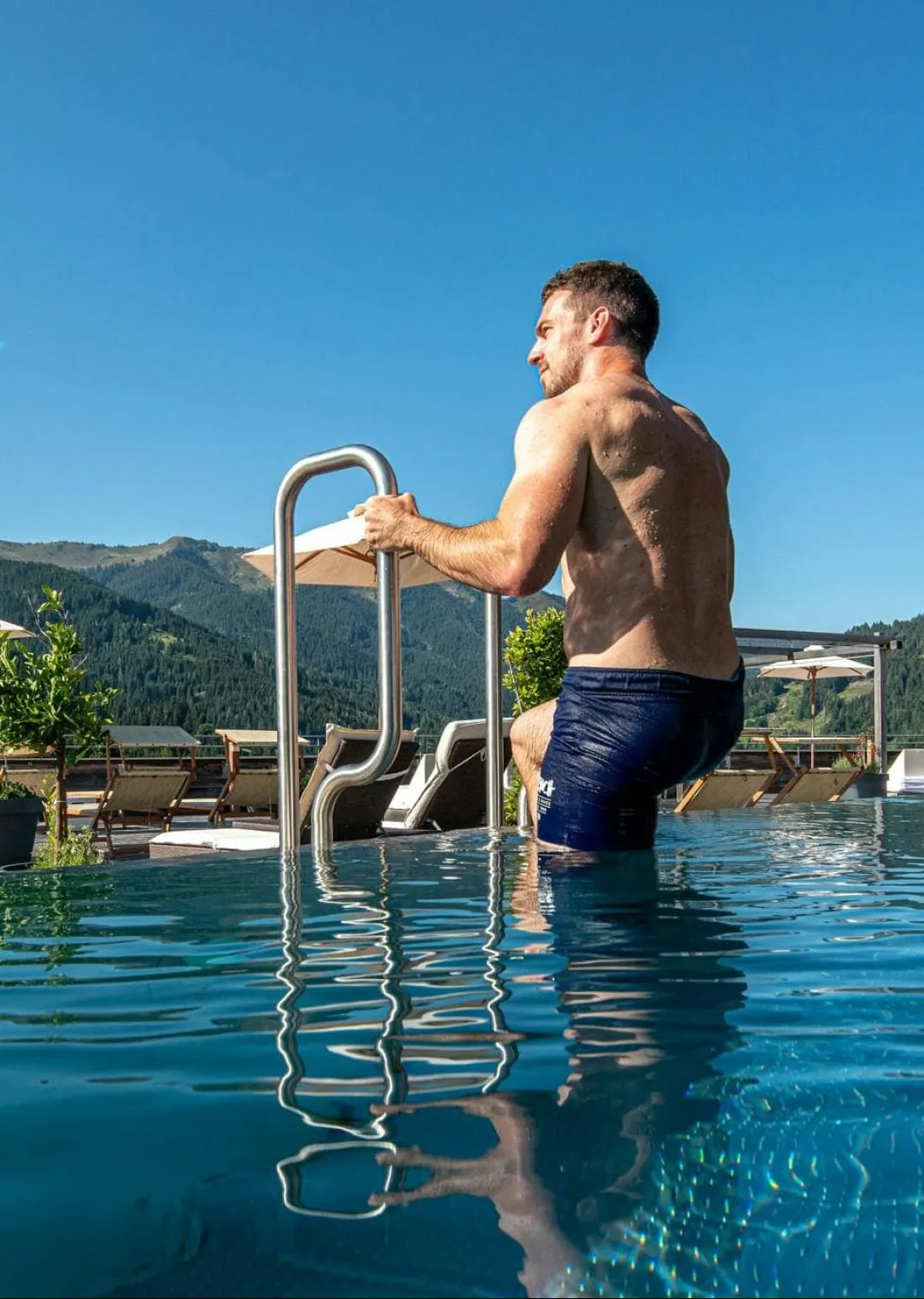 Man emerging from a pool with mountain and lounge chairs view