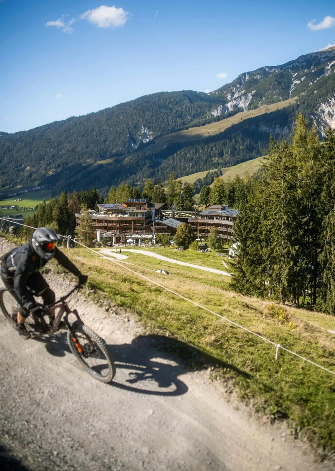 Mountain biker on a trail in a mountainous landscape with trees and buildings.