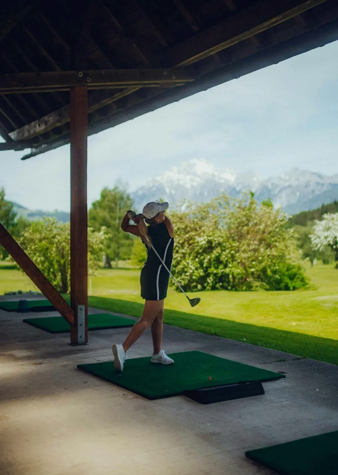 Woman swinging a golf club on a driving range with mountains in the background