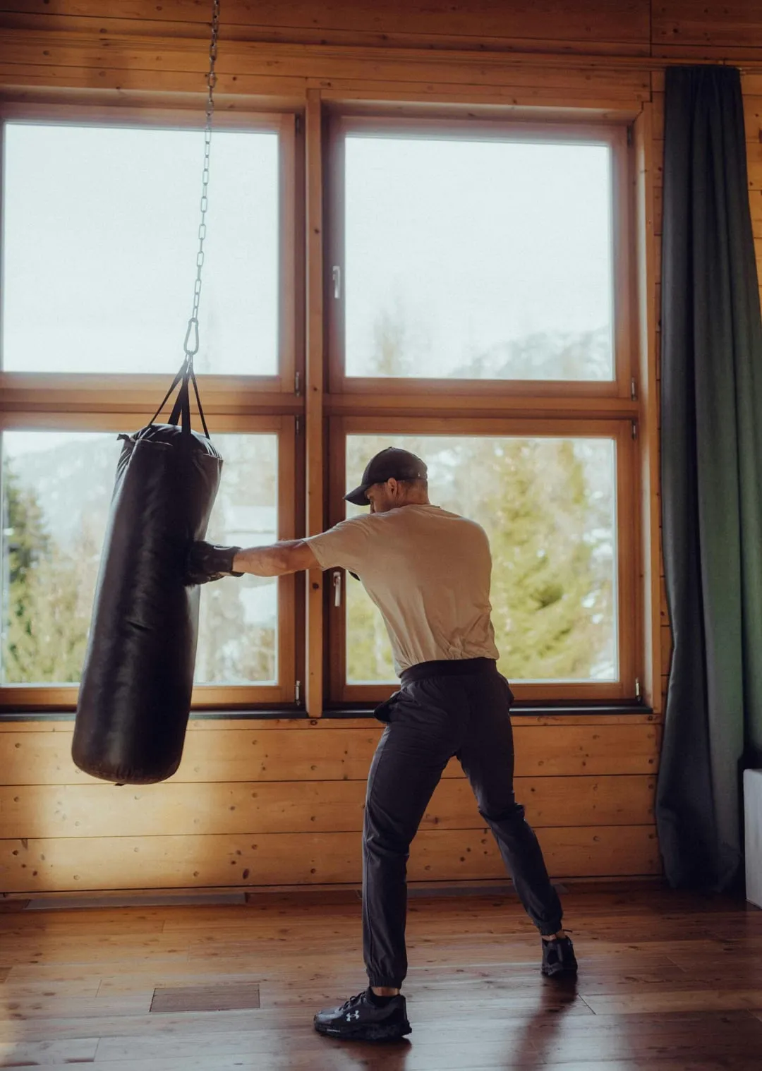 Man punches a punching bag in a bright room with windows.