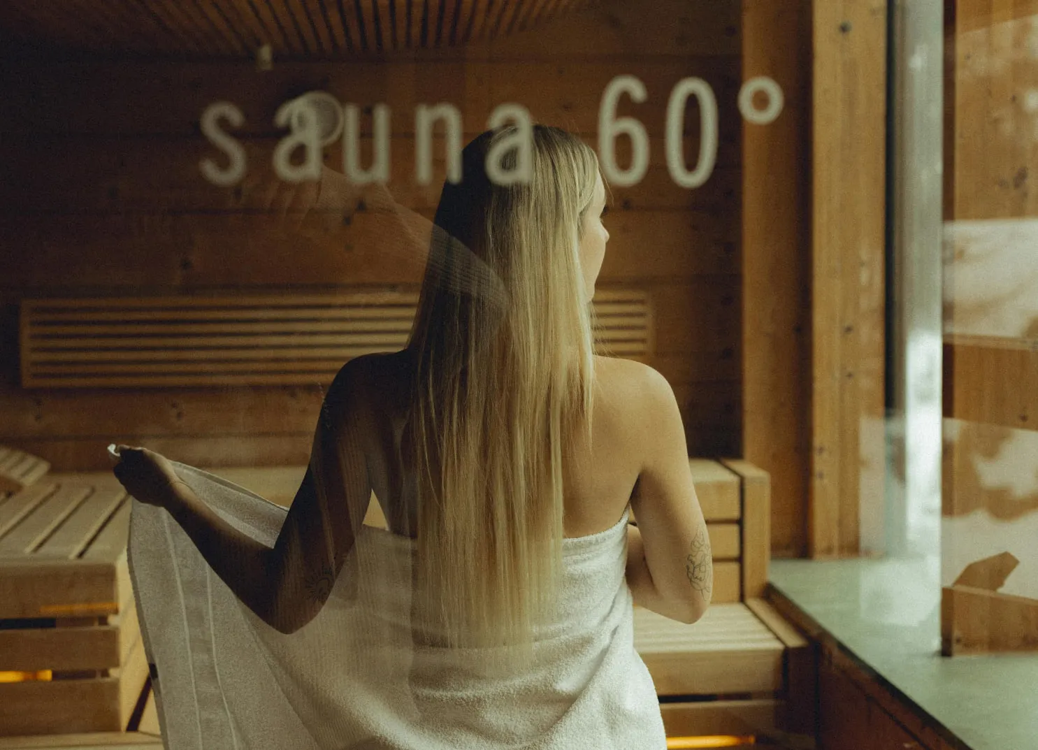 Frau in der Sauna mit einem Handtuch, sichtbare Sauna-Temperatur 60°.