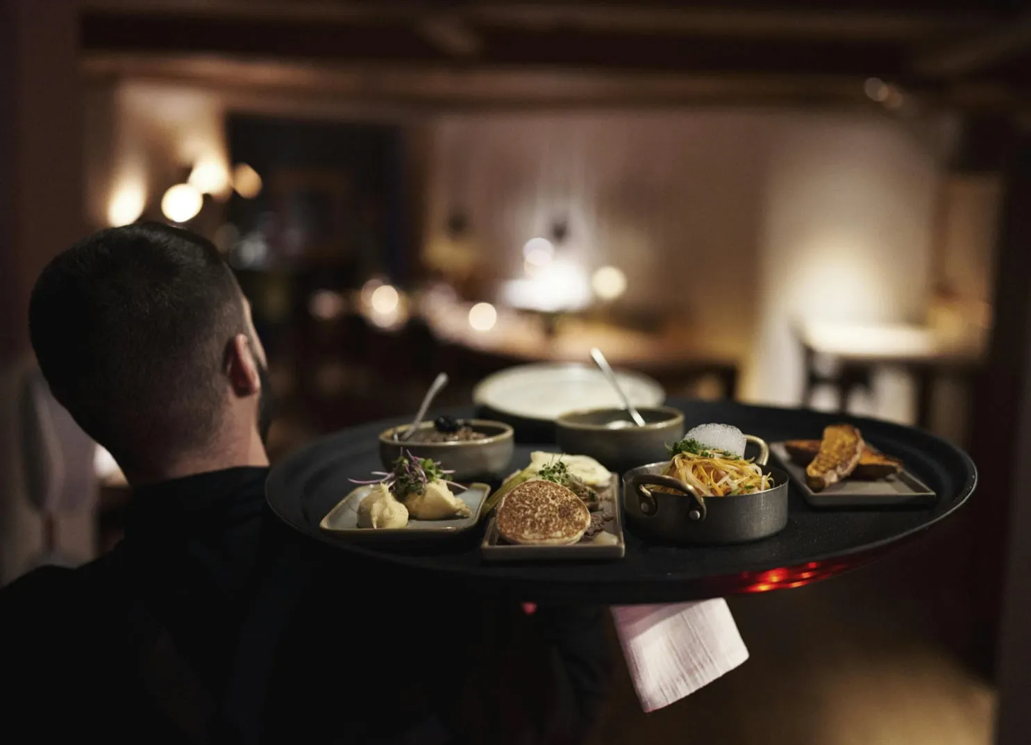 Ein Kellner trägt ein rundes Tablett mit verschiedenen Gerichten in einem Restaurant