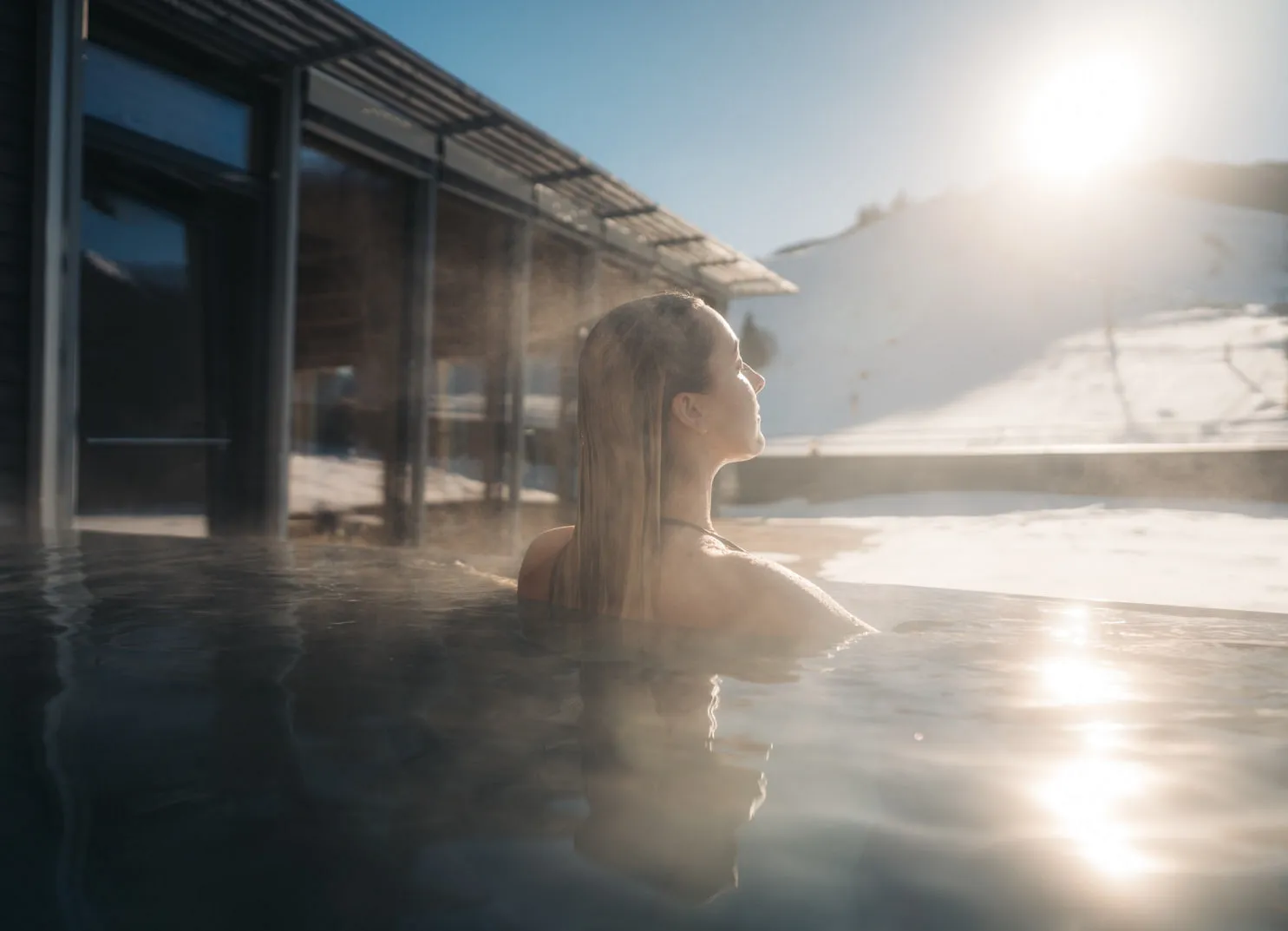 Woman in a swimming pool at Holzhotel Forsth with snow in the background