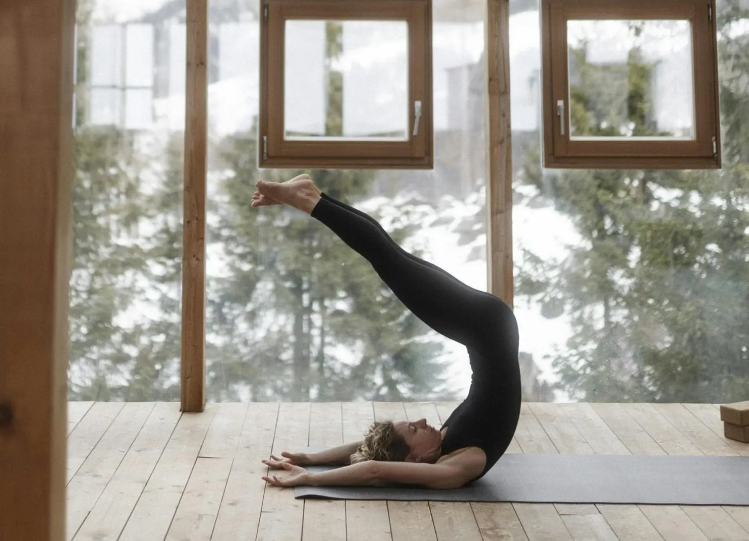 Person practicing yoga in a studio with large windows and wooden floors