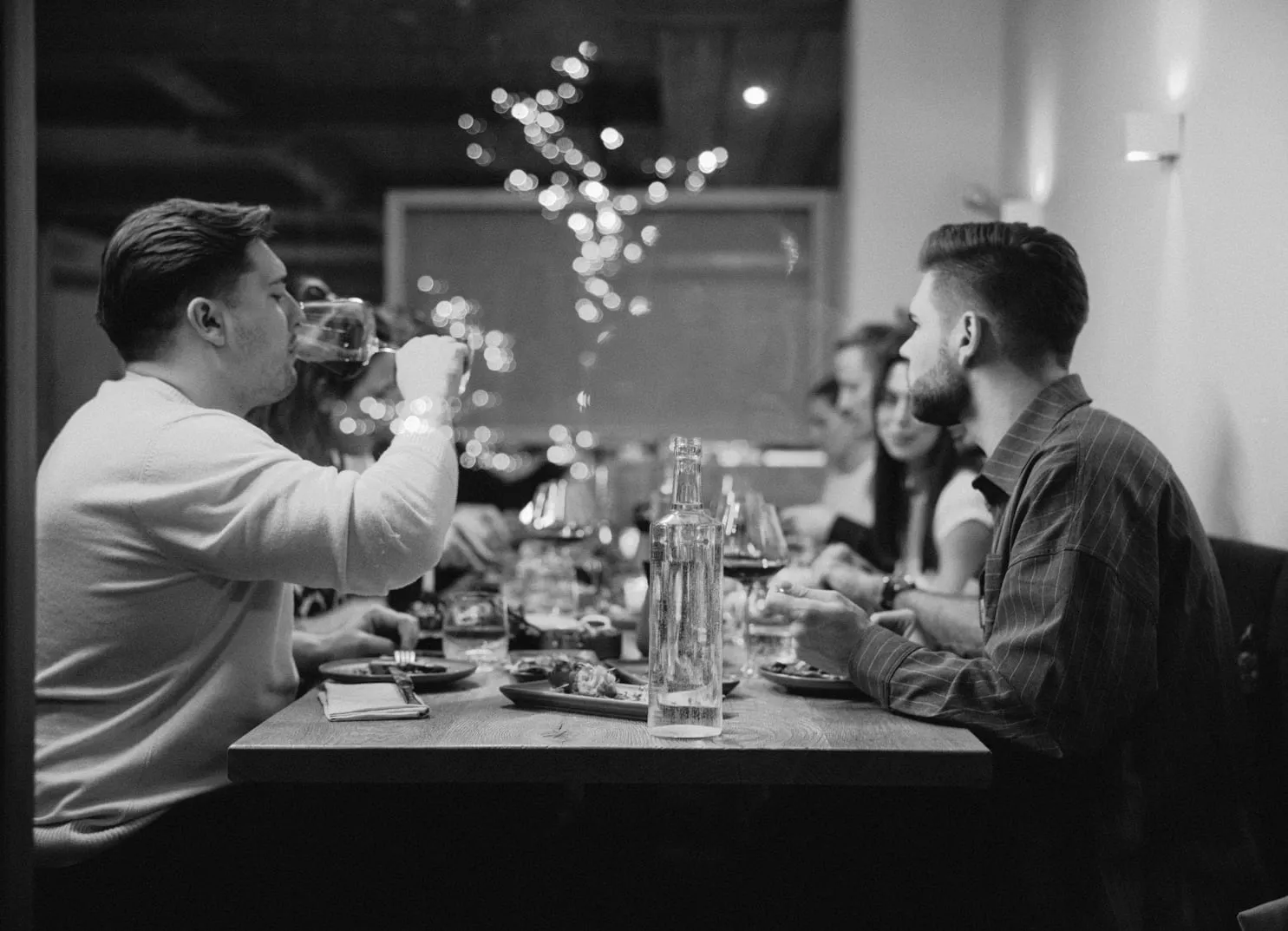 Group of people dining at a table with drinks and food in a cozy setting