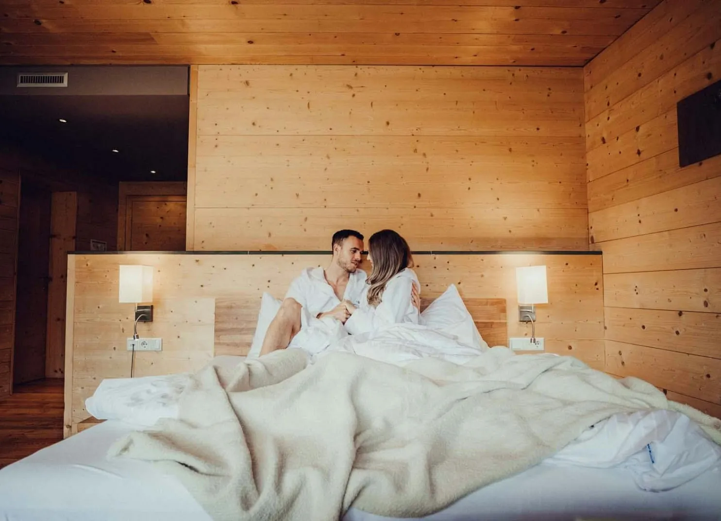couple sitting on a bed in a cozy wooden room, smiling at each other