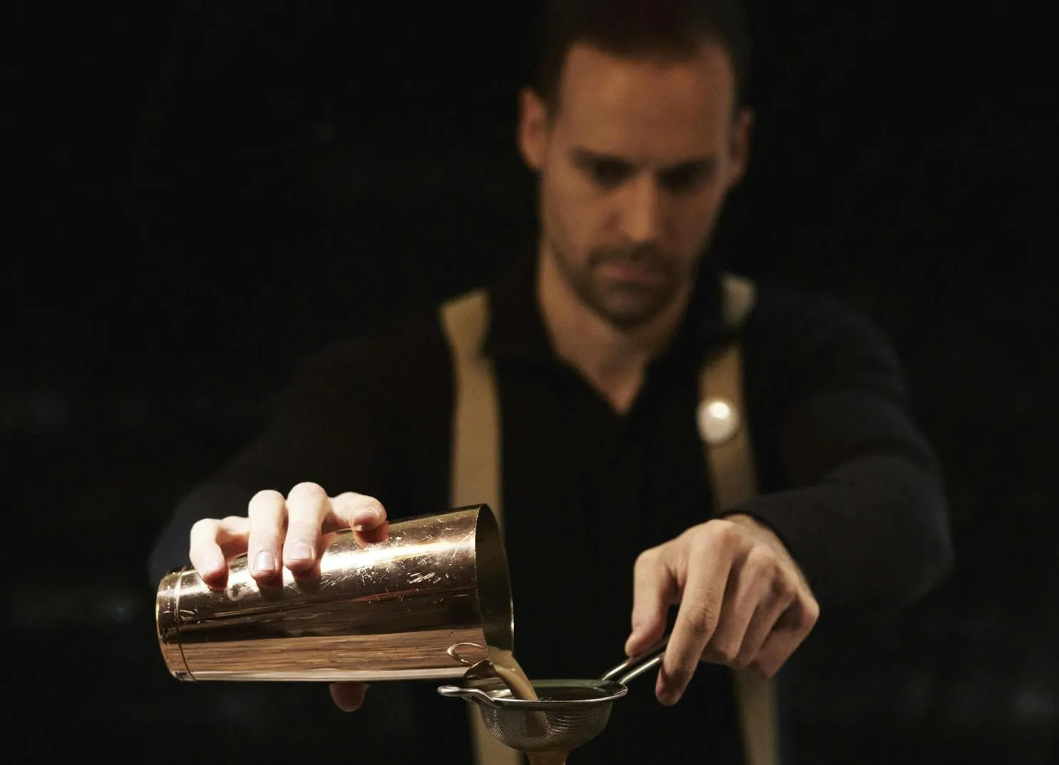 Bartender pouring from a cocktail shaker into a strainer
