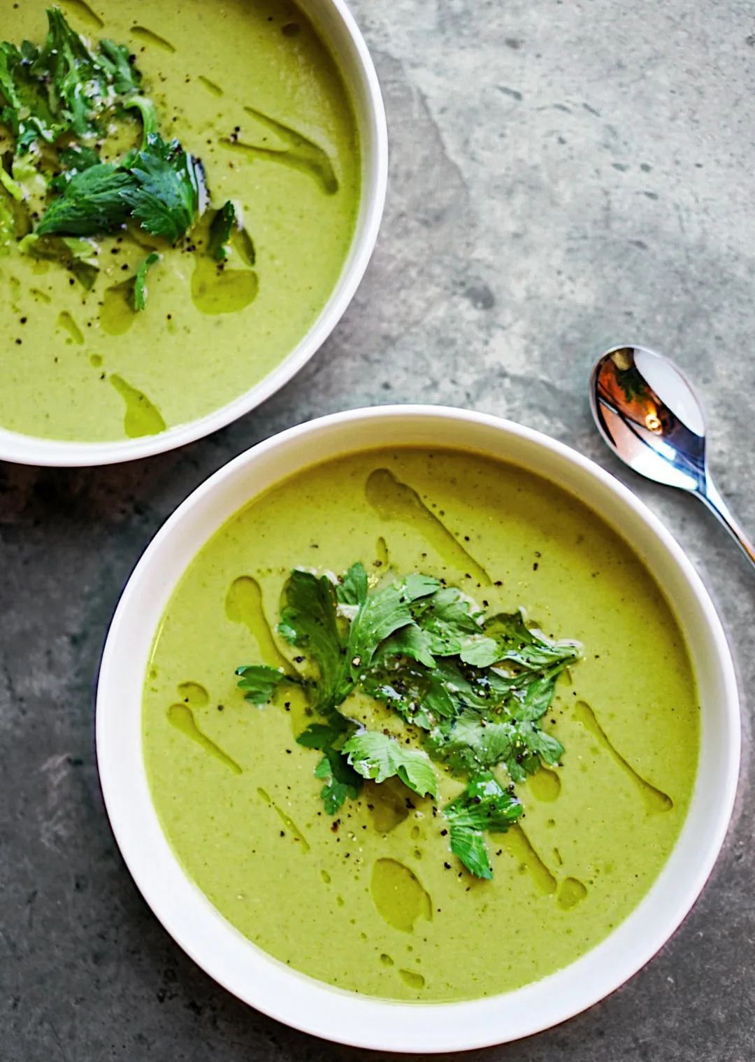 Zwei Schalen mit grüner Suppe, garniert mit frischen Kräutern.