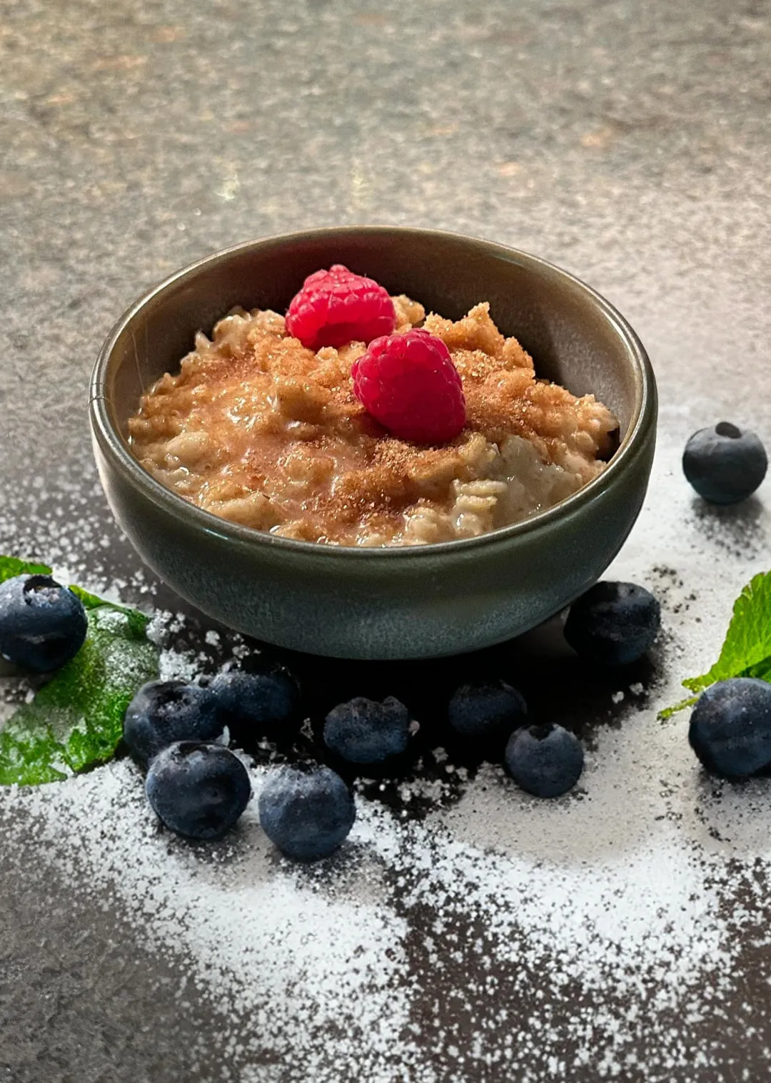 Schüssel mit Haferbrei, Himbeeren und Blaubeeren auf einer dunklen Oberfläche