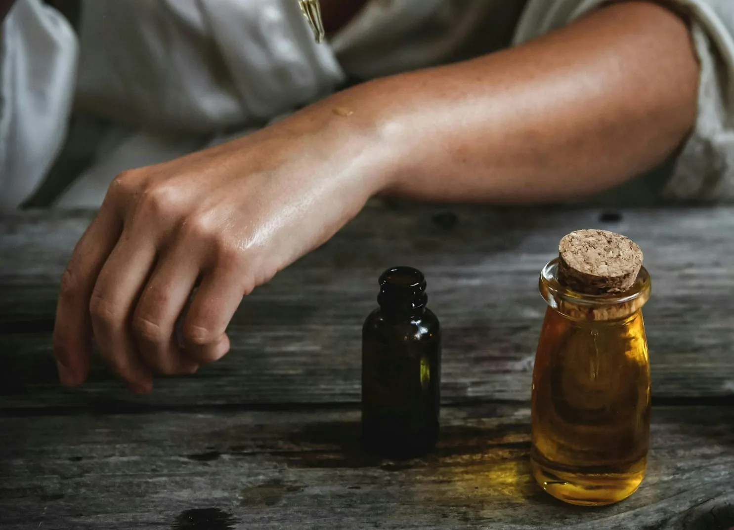 Hand reaching for glass bottle with oil-like contents on wooden surface