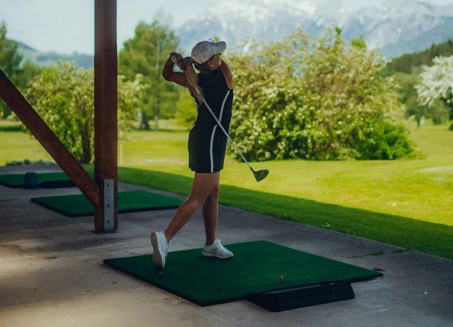 Female Golfer, die auf einer Driving Range mit Bergen im Hintergrund schwingt