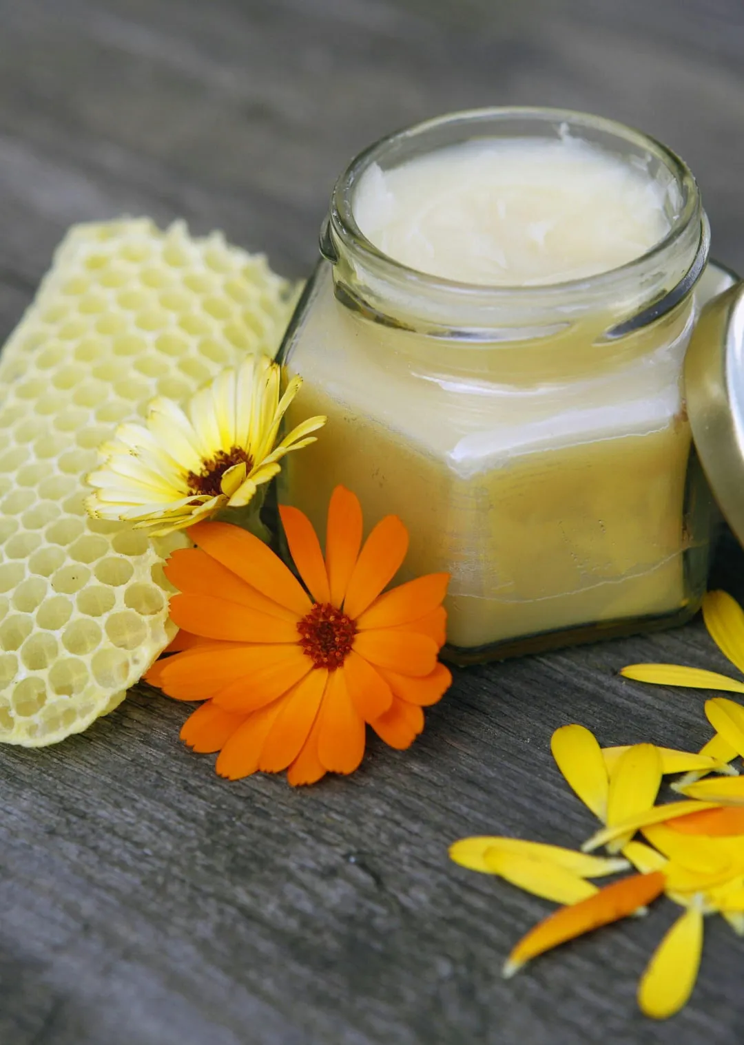 Honeycomb, jar of cream, and marigold flowers on a wooden surface